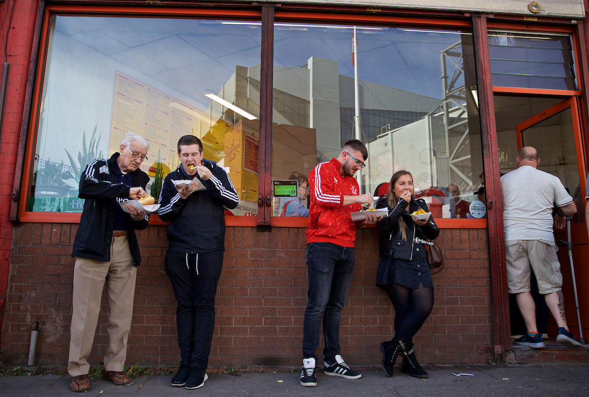 LIVERPOOL, ENGLAND - Saturday, September 14, 2019: Supporters eat a traditional pre-match meal of chips (fried potatoes) outside the Sing Fong Chinese "chippy" with the stadium reflected in the window before the FA Premier League match between Liverpool FC and Newcastle United FC at Anfield. (Pic by David Rawcliffe/Propaganda)