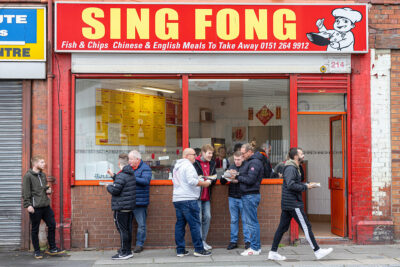 Supporters eat a traditional pre-match meal of chips from the famous Sing Fong Chinese take away outside Anfield